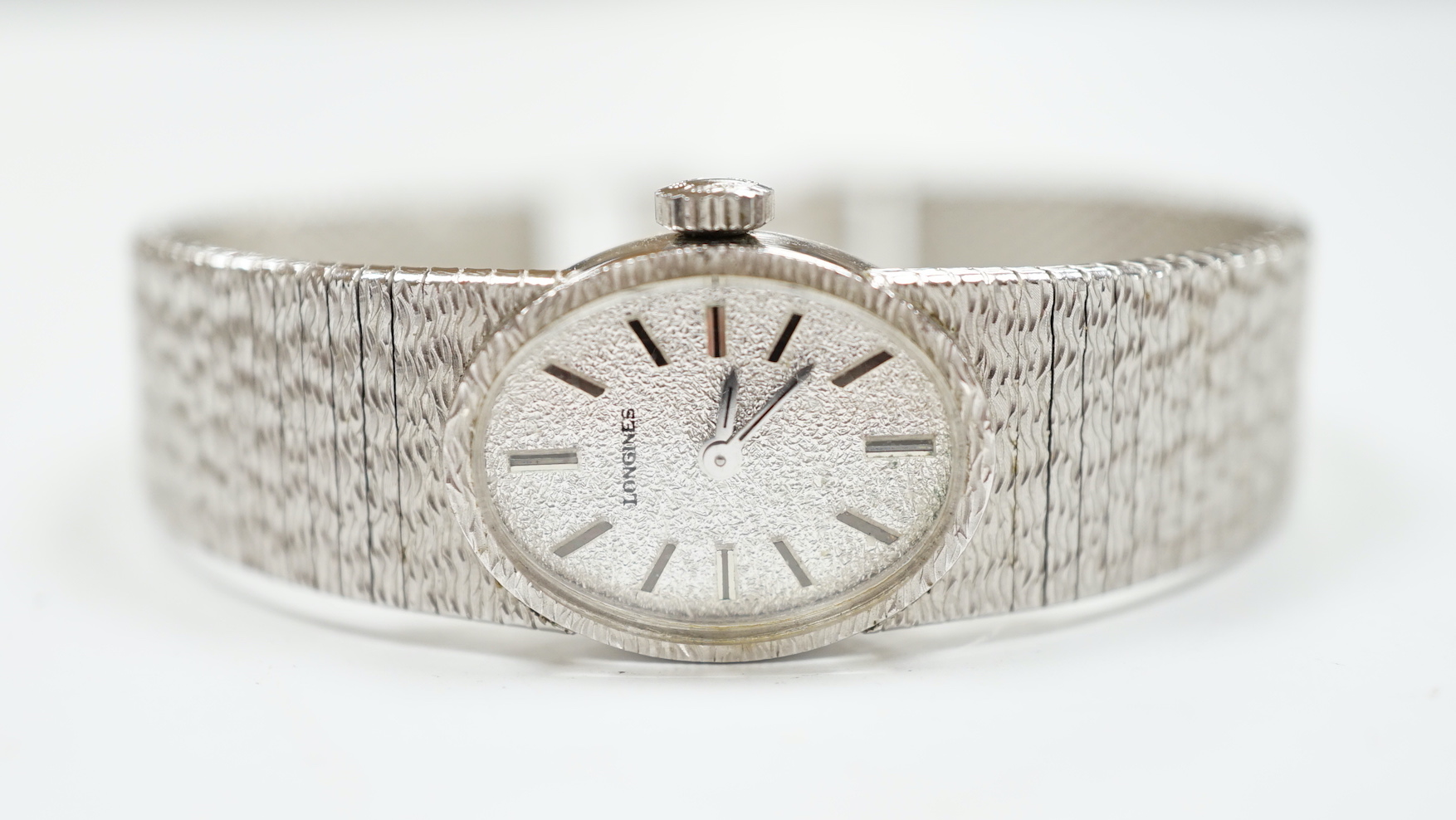 A lady's late 1950's 9ct. white gold Longines manual wrist watch, with integral 9ct white gold bark effect bracelet, gross weight 32.1 grams, with Longines box, no papers.